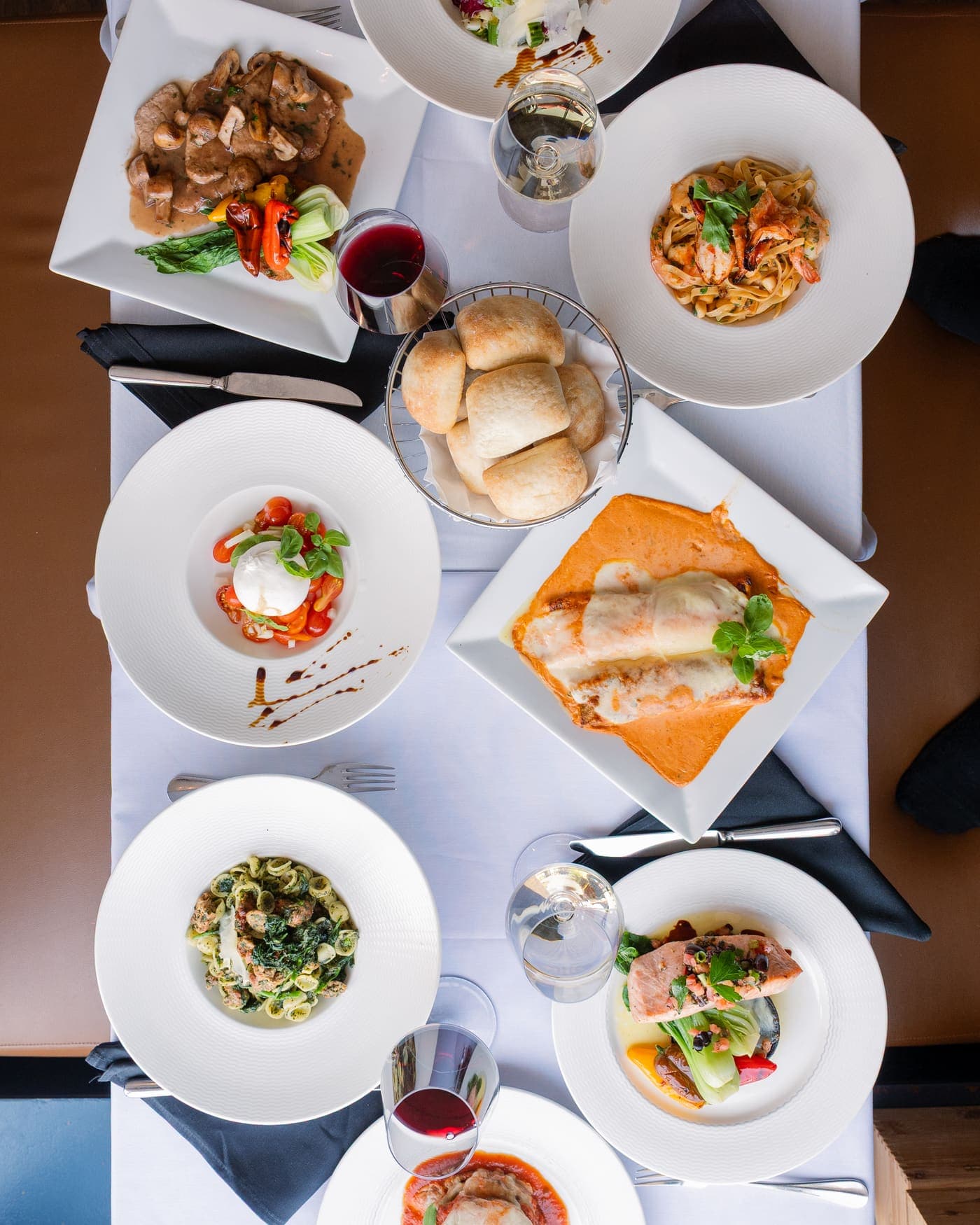 Table vue du dessus : burrata, fettuccine aux crevettes, cannelloni gratinés, orecchiette, saumon, pain et verres de vin
