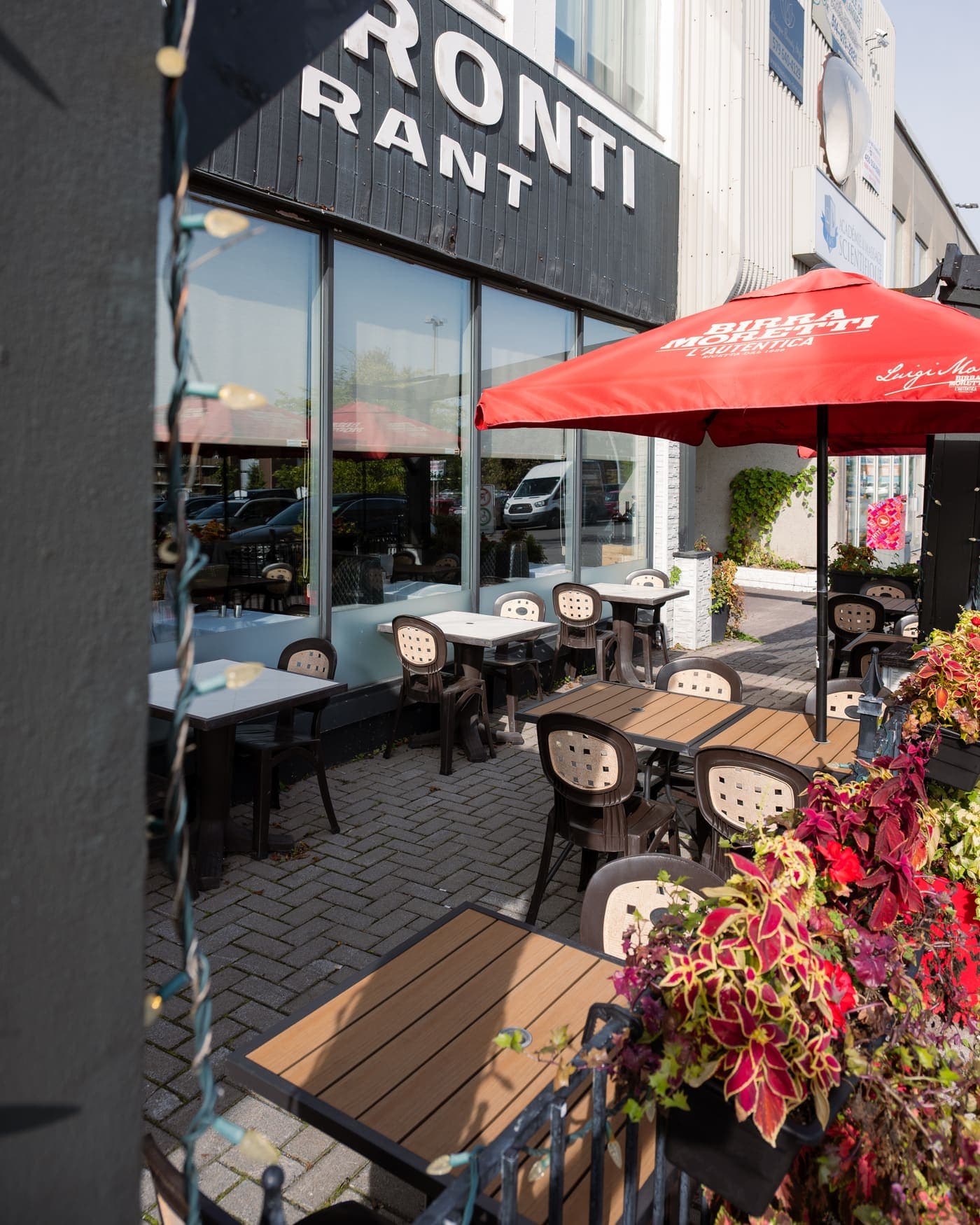 Terrasse devant le restaurant : tables en bois, parasol rouge et jardinières fleuries